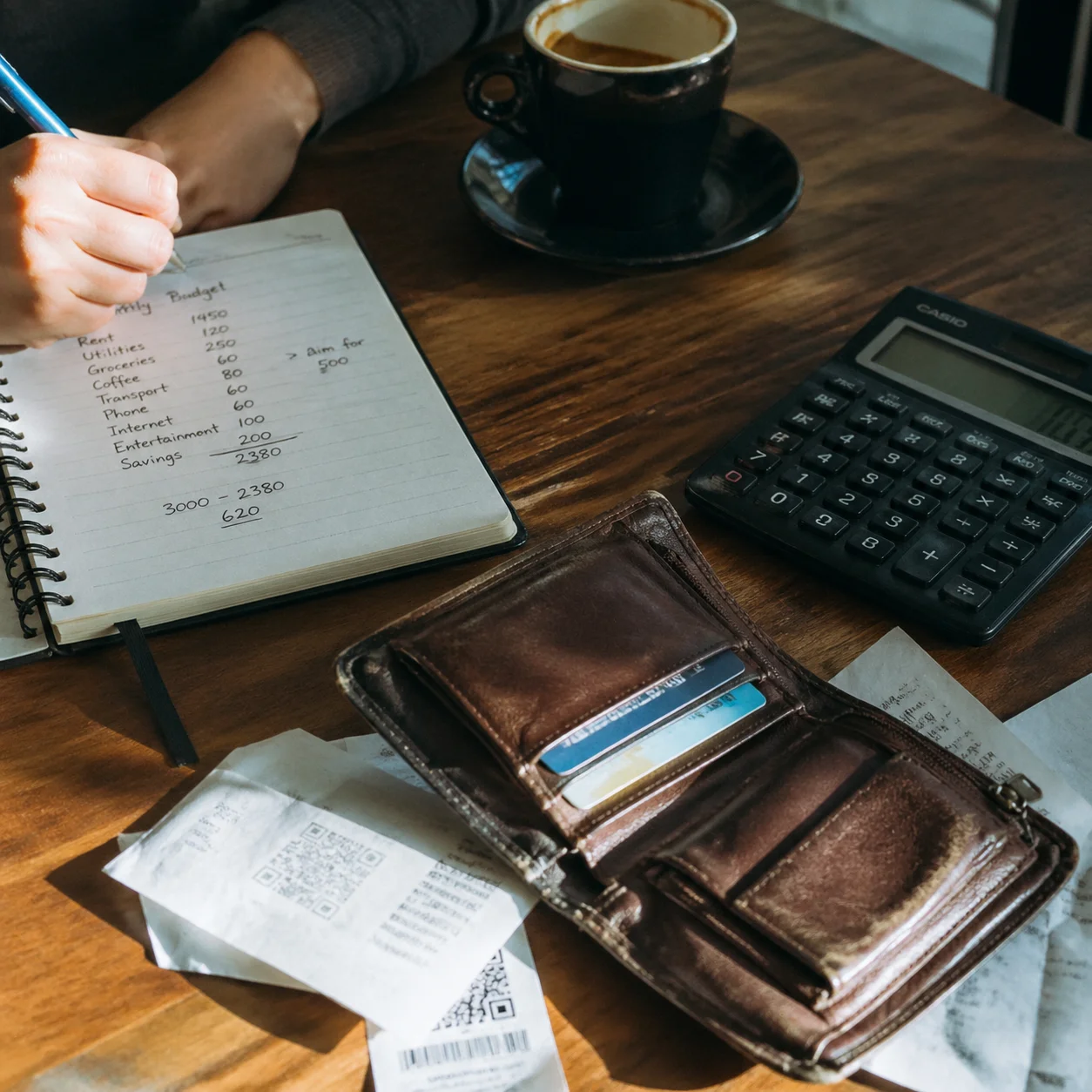 Open wallet beside a handwritten budget notebook and calculator on a wooden table, illustrating financial literacy basics